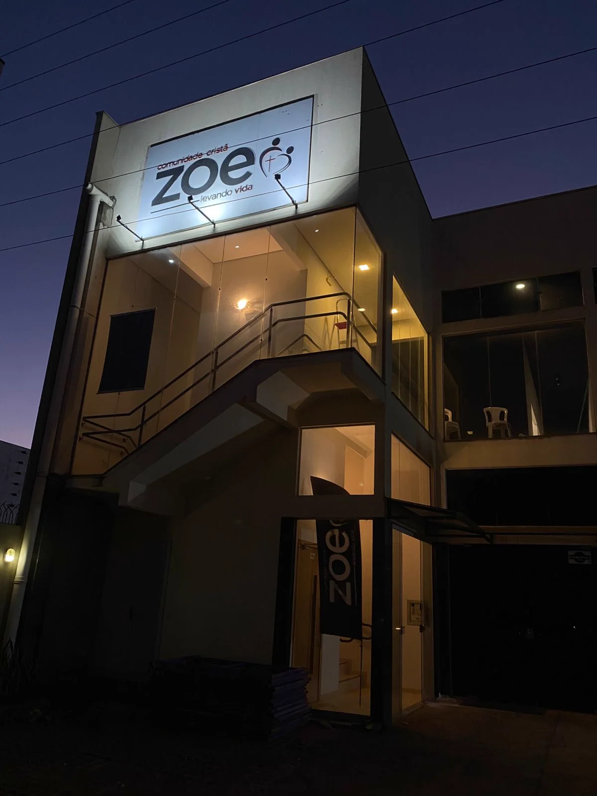 Fachada da Comunidade Cristã Zoe Maringá ao entardecer, com o letreiro aceso